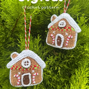 May include: Two crocheted gingerbread house ornaments with white icing, candy cane details, and red and white striped hanging strings. The ornaments are set against a backdrop of green foliage. The text "Digital Crochet pattern" is at the top.