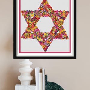 May include: A framed print featuring a Star of David composed of colorful flowers. The artwork is set against a white background with a pink border, encased in a black frame. The image is displayed above a decorative shelf.