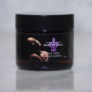 Puede incluir: Un frasco negro de exfoliante facial de &aacute;rbol de t&eacute; con tapa negra. La etiqueta presenta la silueta de una mujer y el texto "BODY BY ANCA TEA TREE FACE SCRUB 2 oz."