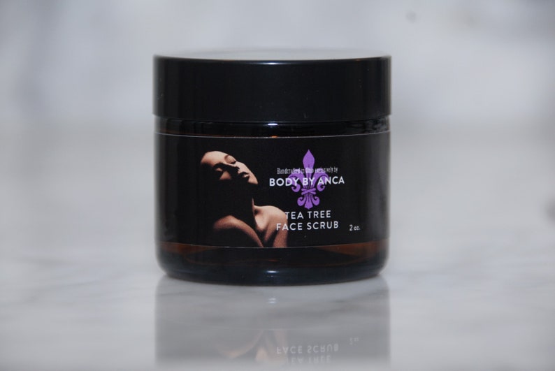 Puede incluir: Un frasco negro de exfoliante facial de &aacute;rbol de t&eacute; con tapa negra. La etiqueta presenta la silueta de una mujer y el texto "BODY BY ANCA TEA TREE FACE SCRUB 2 oz."