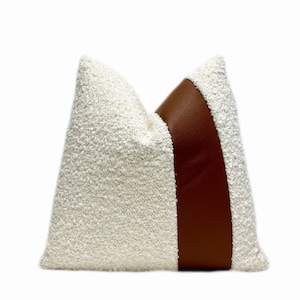 May include: A white and brown throw pillow with a textured fabric and a brown leather accent.