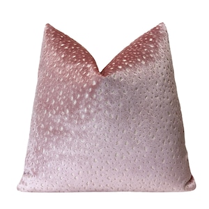 May include: A decorative, dusty rose-colored pillow with a velvet texture. The pillow features a pattern of small, raised dots across its surface. The top of the pillow has a lighter, faded appearance.