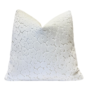 May include: A white decorative pillow with a textured, leopard-like pattern. The pillow is square and has a soft, plush appearance. The pattern is raised, creating a tactile surface.