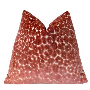 May include: A pink velvet pillow with a white abstract pattern. The pillow is soft and plush, and the pattern is subtle and elegant.