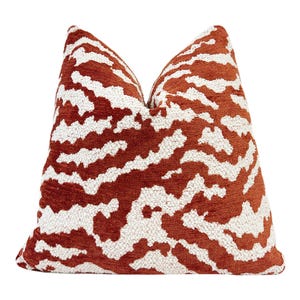 May include: A square throw pillow featuring a textured, two-tone pattern of burnt orange and off-white. The design consists of irregular, abstract shapes that create a wavy, organic appearance across the entire surface of the pillow cover.