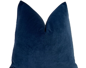 May include: A plush, navy blue velvet pillow. The pillow has a soft, velvety texture and a classic square shape. The deep blue color adds a touch of elegance and sophistication to any room. This decorative pillow is perfect for adding comfort and style to a sofa or bed.