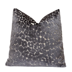 May include: A decorative square pillow with a dark gray, textured pattern. The pattern consists of small, irregular circles, creating a spotted or leopard-like design. The pillow has a soft, velvety appearance and is likely made of a plush fabric.