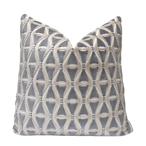 May include: A square decorative pillow with a geometric pattern. The pillow features a repeating design of interlocking shapes in a light gray and off-white color scheme. The pillow is made of a soft, textured fabric.