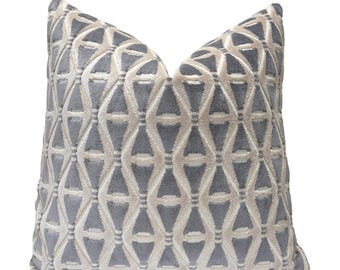 May include: A square decorative pillow with a geometric pattern. The pillow features a repeating design of interlocking shapes in a light gray and off-white color scheme. The pillow is made of a soft, textured fabric.