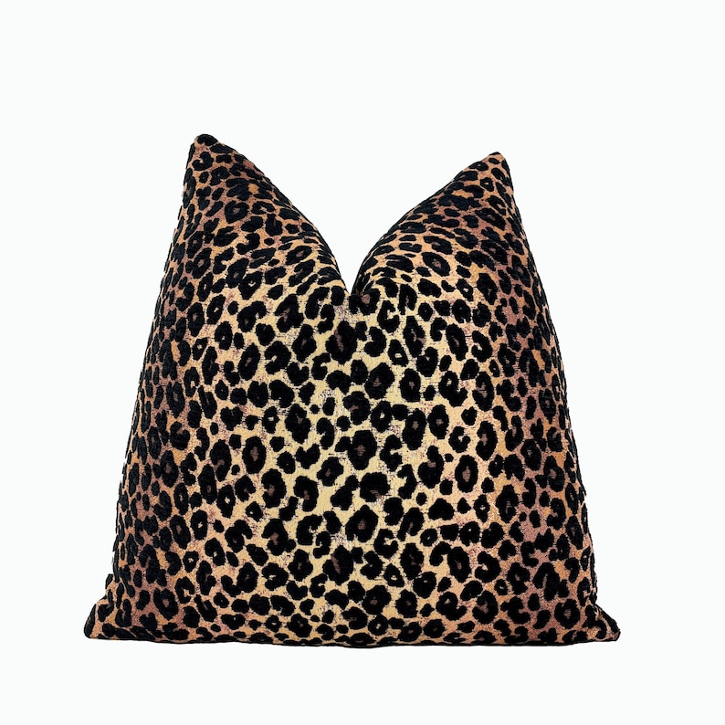 Puede incluir: Una almohada de tiro de estampado de leopardo negro, marr&oacute;n y naranja. La almohada est&aacute; hecha de una tela suave y mullida.