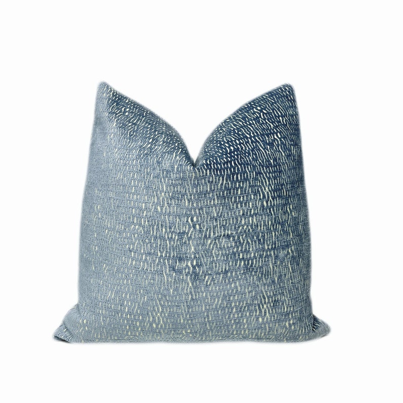 May include: A square cushion with a textured, woven design. The cushion displays a gradient of blue shades, shifting from a lighter tone in the middle to a darker colour towards the borders. This cushion is intended for home decoration.