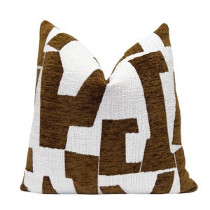 May include: A decorative throw pillow with a geometric pattern. The pillow features a textured fabric with a repeating design of brown shapes against a white background. The pillow is square and has a soft, inviting appearance.