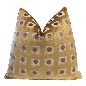 May include: A gold velvet pillow with a geometric pattern of squares and circles. The squares are outlined in a lighter gold color and the circles are a darker brown color.