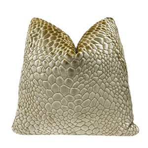 May include: A decorative pillow with a textured, reptile-like pattern in shades of beige and gold. The pillow has a soft, velvety appearance and a rounded shape, perfect for adding a touch of luxury to any room.
