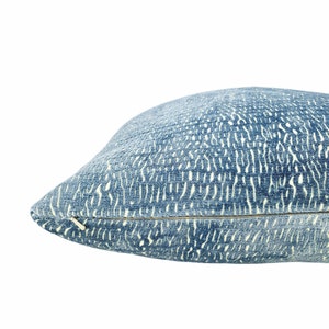 May include: A blue cushion with a textured pattern and a zip closure. The cushion has a light blue background with a white pattern. The cushion is a home decor item.