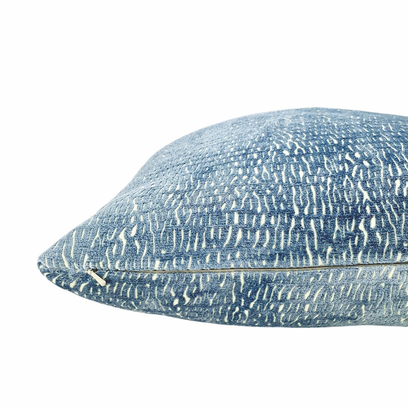 May include: A blue cushion with a textured pattern and a zip closure. The cushion has a light blue background with a white pattern. The cushion is a home decor item.