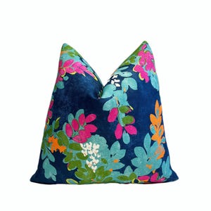 May include: A decorative throw pillow with a vibrant floral pattern. The pillow features a dark blue background with colorful flowers in shades of pink, teal, green, and orange. The pillow is square-shaped and has a soft, textured appearance.
