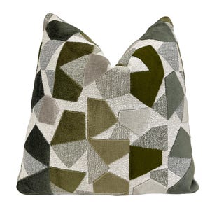 May include: Decorative throw pillow with a geometric pattern. The pillow features a patchwork design with various shades of green, gray, and white. The shapes include triangles, rectangles, and irregular polygons. The pillow has a soft, textured appearance and is likely made of fabric.