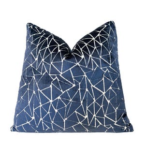 May include: Navy blue decorative pillow with a geometric pattern. The pillow features a dark blue background with a white triangular design. The pillow is square and has a soft, velvety texture.