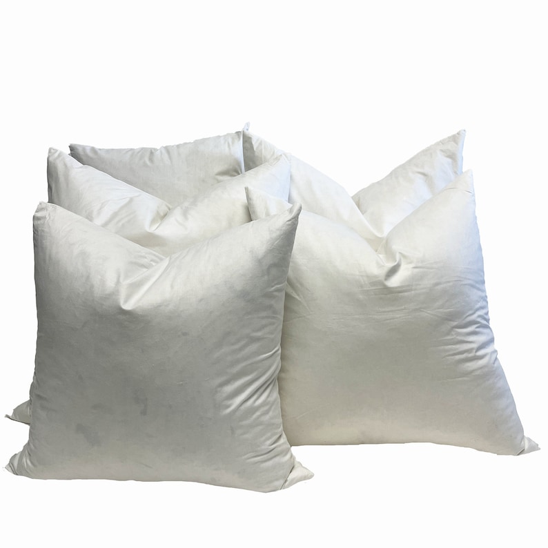 May include: Several white square pillows are arranged against a white background. The pillows have a soft, puffy appearance, with visible seams and a slightly textured surface. The pillows are likely for home decor or bedding.