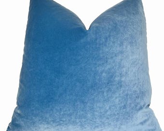May include: A soft, blue velvet pillow with a square shape. The pillow is made of a plush, textured fabric.