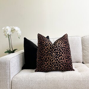 Puede incluir: Un sof&aacute; blanco con dos cojines. Un coj&iacute;n es negro y el otro es de estampado de leopardo marr&oacute;n y negro.
