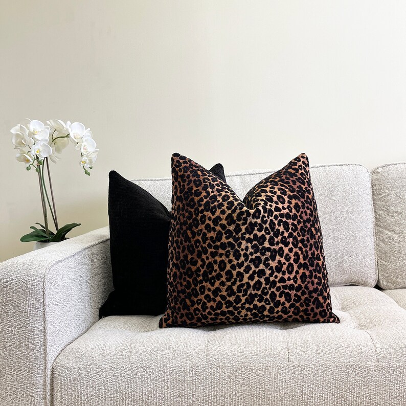 Puede incluir: Un sof&aacute; blanco con dos cojines. Un coj&iacute;n es negro y el otro es de estampado de leopardo marr&oacute;n y negro.