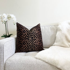 Puede incluir: Un sof&aacute; blanco con un coj&iacute;n de estampado de leopardo negro y marr&oacute;n y una manta de piel sint&eacute;tica blanca.