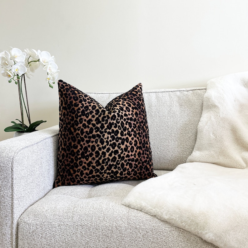 Puede incluir: Un sof&aacute; blanco con un coj&iacute;n de estampado de leopardo negro y marr&oacute;n y una manta de piel sint&eacute;tica blanca.