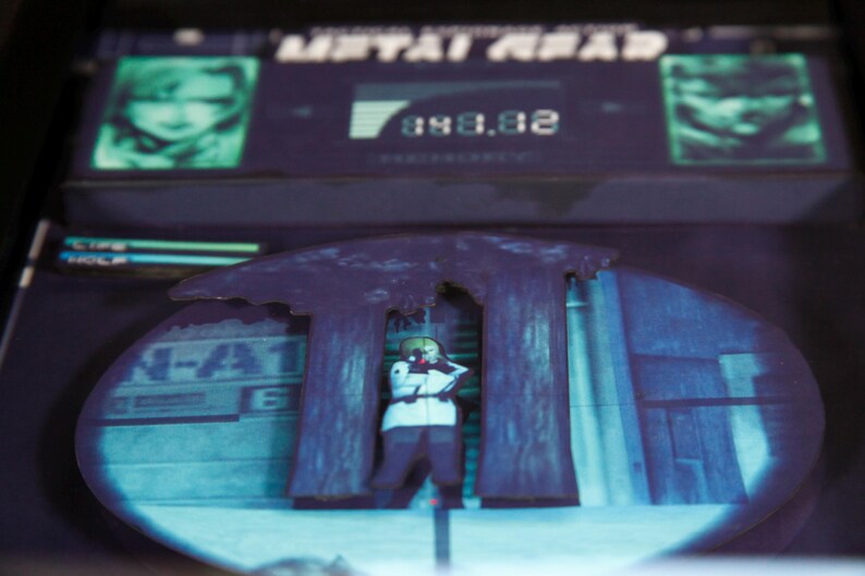 May include: A blue and purple video game screen with the text "METAL GEAR" and a character in a white suit standing in front of two large trees. The screen displays the number "080.02".