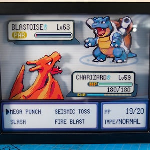 May include: A framed image of a video game battle between a red Charizard and a blue Blastoise. The Charizard is at level 59 with 180/180 HP. The Blastoise is at level 63. The Charizard has the moves Mega Punch, Slash, Seismic Toss, and Fire Blast. The PP for the moves is 19/20. The type is Normal.