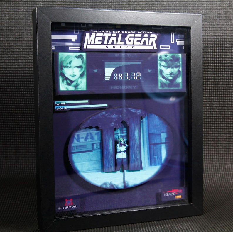 May include: A framed 3D diorama of a scene from the video game Metal Gear Solid. The diorama features a character standing in a hallway with the text "N-A1" and "6" on the wall. The diorama is set in a black frame with the game's title and logo at the top.
