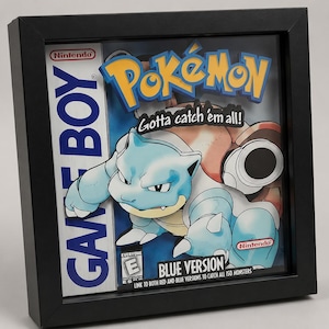May include: A 3D shadow box display featuring the Nintendo Game Boy Pokémon Blue Version game cover art. The artwork includes the blue Blastoise character, the Pokémon logo, the text Gotta catch 'em all!, and the ESRB E rating symbol.