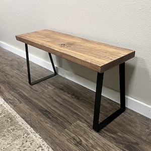 May include: A wooden bench with a natural brown finish and black metal legs. The bench has a simple, modern design and would be a great addition to any home.