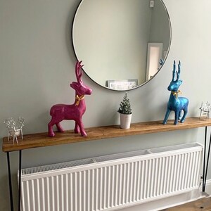 May include: A wooden console table with black hairpin legs, adorned with decorative deer figurines in pink and blue, each with a gold ribbon. A small potted Christmas tree and a round mirror complete the decor.