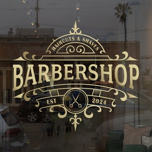 May include: Gold barbershop sign with ornate lettering and a banner reading "EST 2024" with a pair of scissors in the center. The sign is on a storefront window with a reflection of a palm tree and a car.