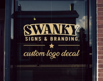 Pode incluir: Vinil decorativo dourado para janela com o texto "SWANKY SIGNS & BRANDING", uma estrela e as palavras "custom logo decal". A janela está numa loja com fachada de tijolo.