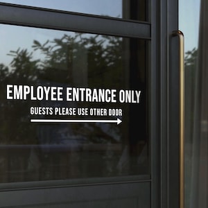 May include: A glass door with the text "EMPLOYEE ENTRANCE ONLY" in white, with the text "GUESTS PLEASE USE OTHER DOOR" below it. A white arrow points to the right. The door has a gold handle and a dark frame.