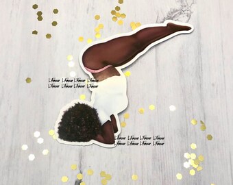 May include: A sticker featuring a stylized illustration of a person in a handstand pose. The figure is depicted with brown skin, wearing a white top and pink underwear. The sticker has the text "L'Amour" repeated multiple times.