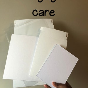 May include: A hand holding a stack of white packaging materials, including paperboard and resealable bags. The text "Packaging with care" is written in black above the packaging.