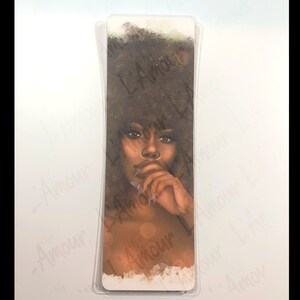 May include: A bookmark featuring a portrait of a woman with dark skin and curly brown hair. The woman is depicted with a thoughtful expression, her finger touching her lips. The bookmark has a clear plastic protective layer.