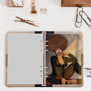 May include: A beige planner with a portrait of a woman with brown hair and a black jumpsuit. The planner has a light gray interior and rose gold rings. The text "***Accessories NOT Included" is visible on the right side of the planner.