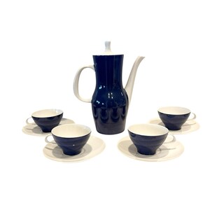 May include: A vintage coffee set featuring a navy blue coffee pot with a white handle and spout, and four matching cups and saucers. The cups and pot have a navy blue exterior and white interior. The set is on a white background.