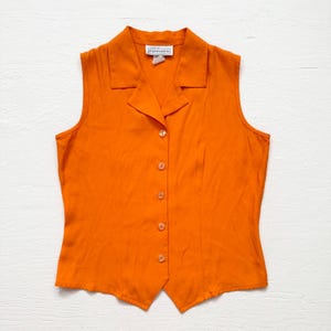May include: Orange sleeveless button-down vest with a collared neckline. The vest has a tailored fit and features a series of small, round buttons down the front. The tag reads "petite impressions".