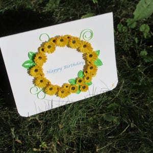 May include: A white card with a yellow and green paper flower wreath and the text "Happy Birthday".