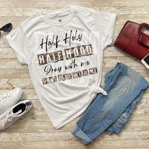 May include: White t-shirt with the text "Half Holy Half Hood Pray with me Don't play with me" printed on it in black with a leopard print background.