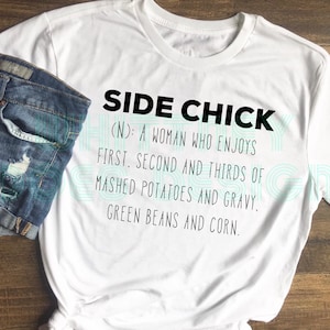 May include: White t-shirt with black text that reads "Side Chick (N): A woman who enjoys first, second and thirds of mashed potatoes and gravy. Green beans and corn."