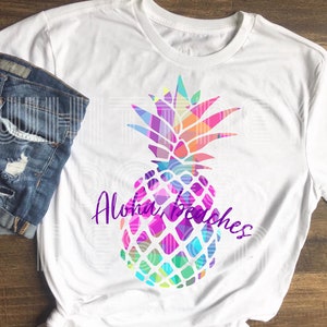 May include: White t-shirt with a colorful geometric pineapple design and the text "Aloha Beaches" in purple.