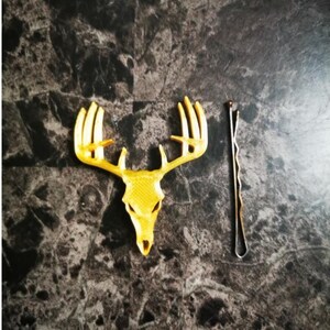 May include: A gold-colored deer skull with antlers, and a gold-colored bobby pin.