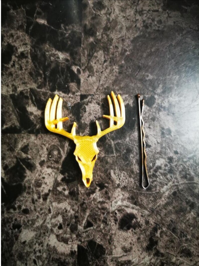 May include: A gold-colored deer skull with antlers, and a gold-colored bobby pin.